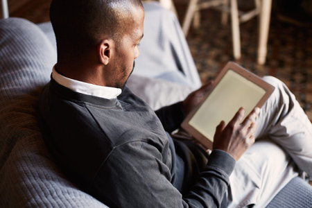 Elegant African black man using tablet on sofa couch in home living room