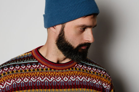 Bearded hipster wearing blue beanie and colored jumper.