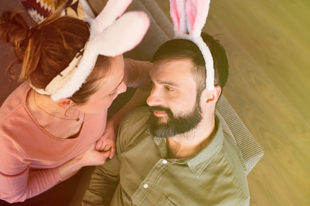Beautiful young loving couple looking to each other with pink rabbit ears on head. Happy family preparing for Easterの写真素材