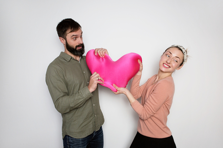 Bearded man and young girl play with red soft toy heart. Couple in love tears big heart on white backgroundの写真素材