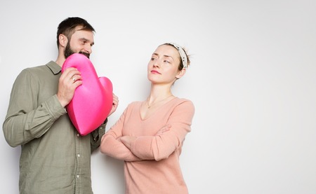 Bearded man and young girl play with red soft toy heart. Couple in love tears big heart on white backgroundの写真素材