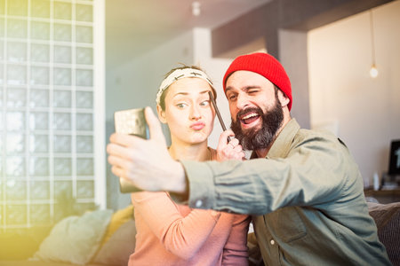 Cheerful young couple taking a humorous selfie with a smartphone. Romantic relationship between...