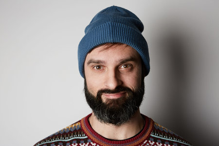 Bearded hipster wearing blue beanie and colored sweater on white background.