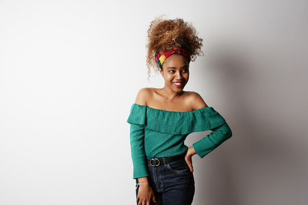 Positive attractive young black african female with Afro hairstyle, points aside with cheerful expression, isolated over bright light backgroud. Advertisement and ethnicity.の写真素材