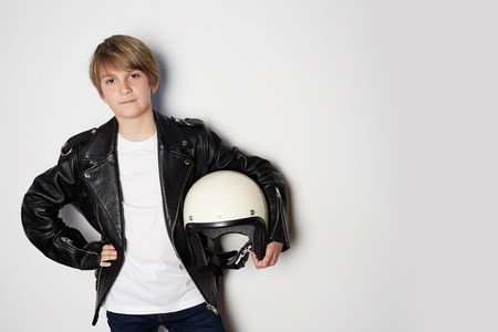 Portrait of Young handsome teen kid in black leather jacket and holding hand white moto helmet smiling on white backgroundの写真素材