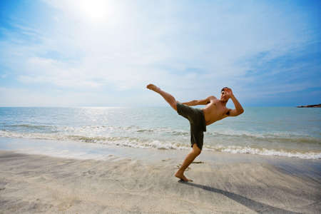 a energetic guy kick boxing by the beach in beautiful skyの写真素材
