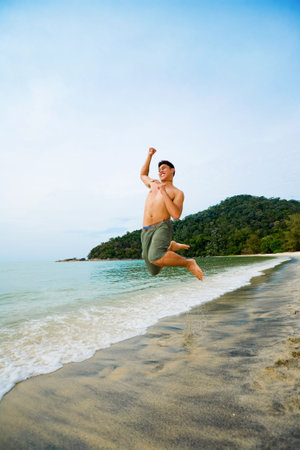 man jumping high up happily on the beachの写真素材