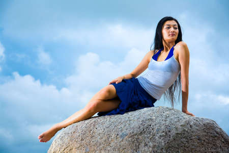 asian woman relaxing on the outdoor rock with blue skyの写真素材