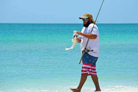 HOLMES BEACH, ANNA MARIA ISLAND, FL - May 1, 2018: A local young man on the beach holding a fish he just caught in the Gulf of Mexico.のeditorial素材