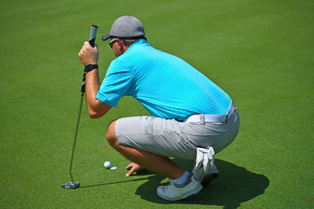 Shallow DOF Image of a Young Man Playing Golf Squatted Down Looking Over the Green before Making His...