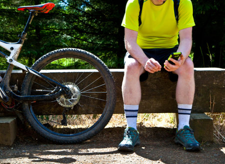 Cyclist sat on a bench next to a bike looking at a phoneの写真素材