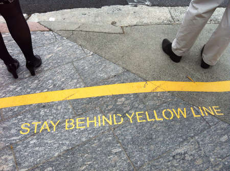 Male and female stand in front of the warning yellow line at the bus stopの素材