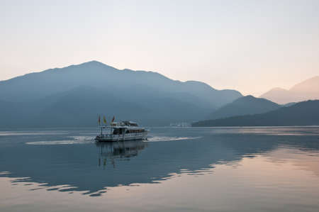 Nantou Taiwan  February 1 2015: A tourist boat is saling calmly in Sun Moon Lake in Nantou province in Taiwan. This photo is taken in the early morning. There is a fog above the mountain with cold temperature.のeditorial素材