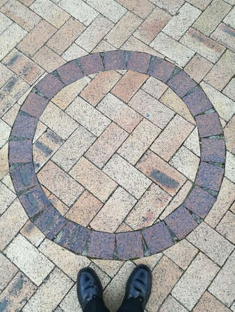 Black leather shoes standing below circle shape cobblestone floorの写真素材