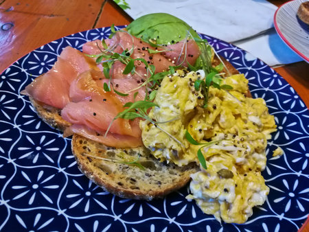 Smoked salmon and healthy scramble eggs on brown hard toast on blue plate in a cafeの写真素材