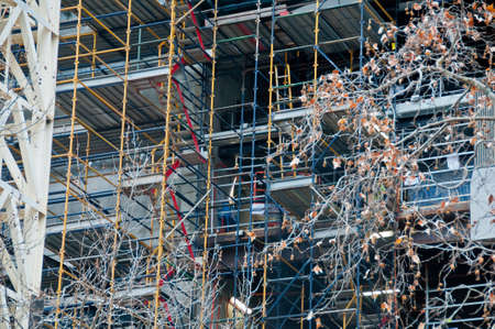 Construction scaffolding of high-rise building and dried leaves tree in Autumnの写真素材