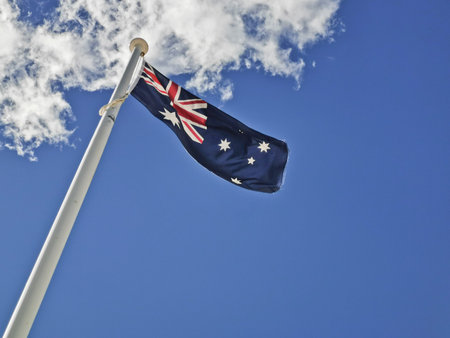 National flag of Australia consists of Union Jack and Southern Cross stars constellation in blue sky sunny day with white cloudの写真素材
