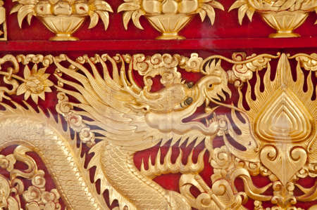 Golden majestic traditional Asian dragon sculpture on dark red wooden wall in templeの写真素材
