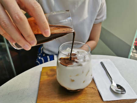 Dirty iced latte pouring espresso shot to white full cream cow milk in cozy coffee shopの写真素材