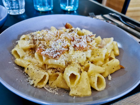 Penne pasta carbonara on white sauce with bacon and extra topping cheese served on blue plateの写真素材