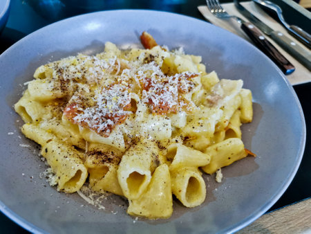 Penne pasta carbonara on white sauce with bacon and extra topping cheese served on blue plateの写真素材