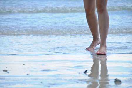 Two legs of lady walking forward on sandy wet beach of the sea with reflectionの写真素材