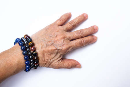 Senior woman's hand wearing supplement good fortune colourful bracelets isolated on white backgroundの写真素材
