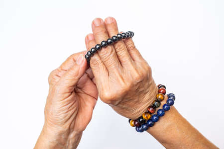 Senior woman's hand wearing supplement good fortune colorful bracelets isolated on white backgroundの写真素材