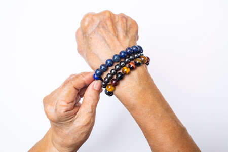 Senior woman's hand wearing supplement good fortune colorful bracelets isolated on white backgroundの写真素材