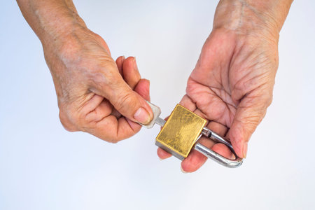 Senior woman's hand hold key unlock master key (Golden padlock ) isolated on white backgroundの写真素材