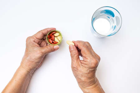 Senior woman's hands holding Vitamin C pills and Antianemia pills in bottle with polka dot glass of water, Healthcare and medical conceptの写真素材