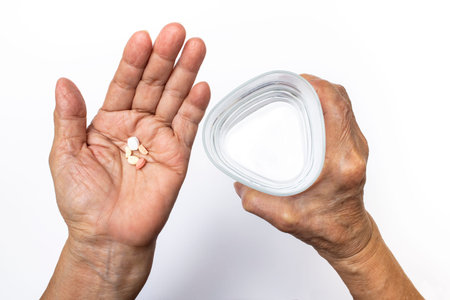 Senior woman's hands holding pills with triangular glass of water, Healthcare and medical concept