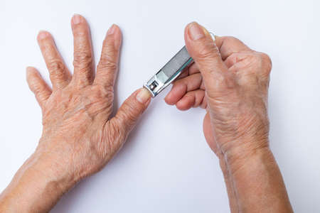 Senior Woman cutting nails using nail clipper isolated on white backgroundの写真素材