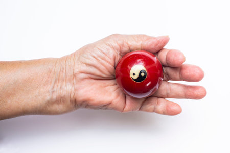 Senior woman's right hand holding a black and white Yin Yang religious symbol on red ball in Taoism isolated on white backgroundの写真素材