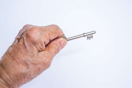 Senior woman's left hand holding key isolated on white backgroundの写真素材