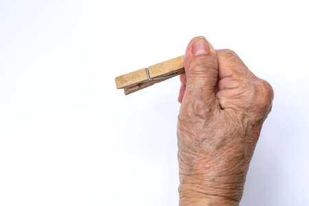 Senior woman's hand holding wooden clothes peg on white backgroundの写真素材