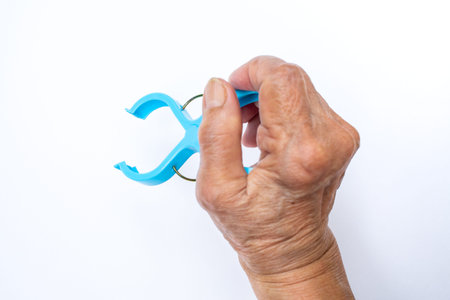 Senior woman's hand squeezing blue plastic clothes peg on white background, Close up shot, Selective...