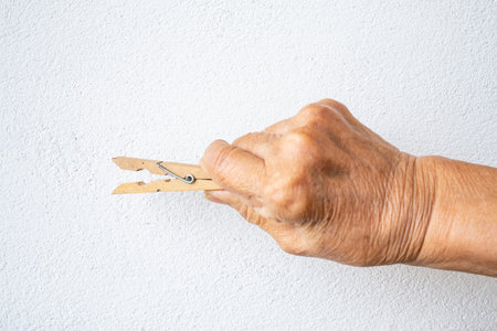 Senior woman's hand holding wooden clothes peg on white background