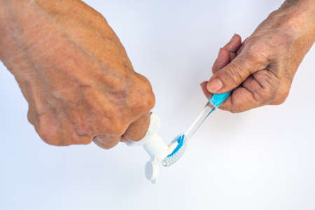 Senior woman's hands squeezing toothpaste on brush against isolated on white backgroundの写真素材