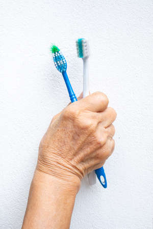 Senior woman's hands holding two old toothbrushes on white backgroundの写真素材