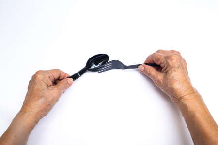 Senior woman's hands holding black plastic spoon and fork isolated on white backgroundの写真素材