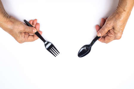 Senior woman's hands holding black plastic spoon and fork isolated on white backgroundの写真素材