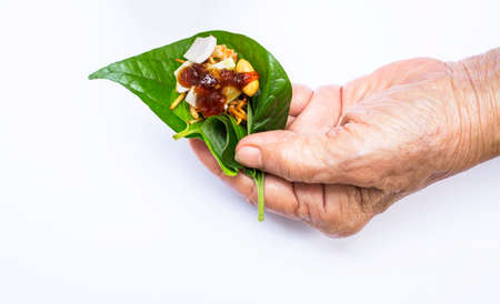 Senior woman's left hand holding Miang Kham isolated on white background, Thai-Style Savory Leaf Wraps (Miang Kham) a traditional snack from Thailandの写真素材