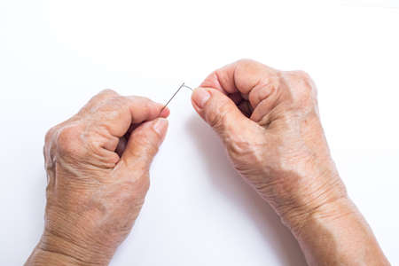 Senior woman's hands trying to thread a needle isolated on white background, About tailorの写真素材