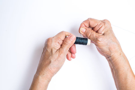 Senior woman's hands spinning to thread roll isolated on white background, About tailorの写真素材