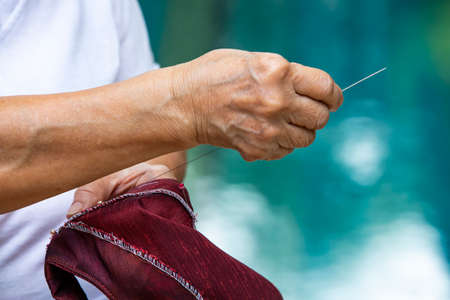Senior woman sewing red silk blouse by hand at swimming pool background , About tailor process, Close upの写真素材