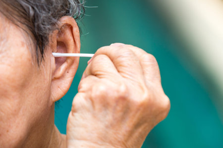 Senior woman's hand holding a cotton swab cleaning her left ear, Close up shot