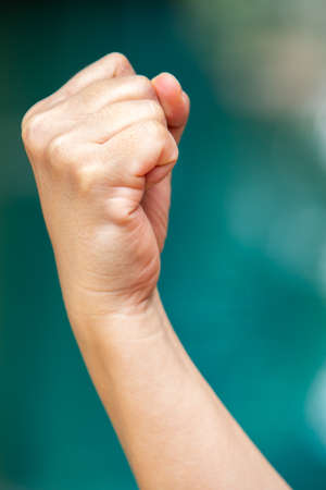 Woman's right hand in fist on bokeh blue swimming pool background, Asian body skin part, Symbol, Gesturing, Body Language Conceptの写真素材