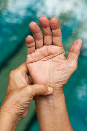 Trigger Finger, Senior woman's left hand massaging her right hand Suffering from pain, Close up and macro shot, Swimming pool background, Health care and massage asian body conceptの写真素材