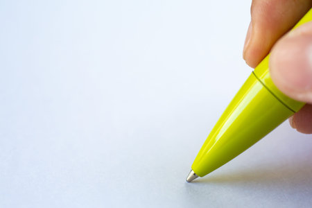 Woman's right Hand holding a green pen, writing letter on white paper background, Notebook, Close up...